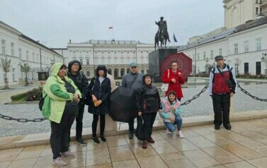 Grupa kobiet i mężczyzn pozuje do zdjęcia. W tle Pałac Prezydencki w Warszawie