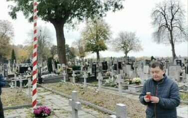 Mężczynza trzymający znicz przy grobach Żołnierzy poległych na cmentarzu wojennym