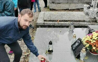 Mężczynza stawiający znicz przy grobach Żołnierzy poległych na cmentarzu wojennym