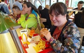 Zdjęcie przedstawia pomieszczenie restauracji McDonald's, w kt&oacute;rym przy stole siedzą dwie kobiety i mężczyzna i konsumują posiłki.
