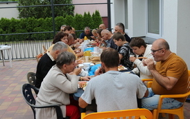 Na zdjęciu grupa kobiet i mężczyzn siedzących na tarasie przy stołach jedzących śniadanie