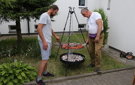 Na zdjęciu dw&oacute;ch mężczyzn stojących przy grillu