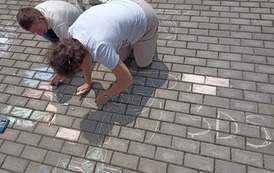 Na zdjęciu kobieta i mężczyzna malujący kredą na kostce brukowej