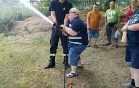 Na zdjęciu mężczyzna lejący mała sikawką strazacką do celu