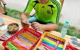 Mężczyzna siedzący przy stole na kt&oacute;rym w pojemnikach leżą kolorowe paski z papieru 