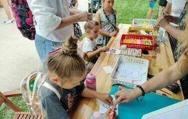 Na zdjęciu trzy dziewczynki siedzące przy stole i wyklejające gotowe wzory metodą quillingu. Na stole leżą w pojemnikach m.in. kolorowe paski papieru, kleje, igły do quillingu, gotowe wzory do wyklejania.