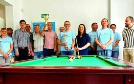 Na zdjęciu grupa kobiet i mężczyzn stojąca przy stole bilardowym