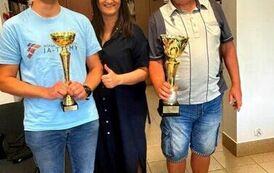 Na zdjęciu dw&oacute;ch mężczyn z pucharami, pomiędzy nimi stoi kobieta