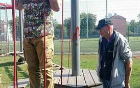 Uśmiechnięty mężczyzna stojący na sprzęcie do ćwiczeń, obok stoi drugi mężczyzna