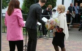 Na zdjęciu dwie kobiety i mężczyzna, jedna z nich wręcza upominek mężczyźnie