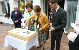 Zdjęcie przedstawia dwie kobiety i dw&oacute;ch mężczyzn przey dużym okolicznościowym torcie, kobiety kroją kroi tort