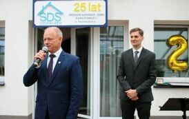 Na zdjęciu dw&oacute;ch mężczyzn w garniturach, jeden z nich przemawia do mikrofonu