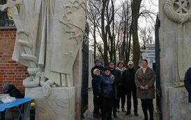 Zdjęcie przedstawia grupę os&oacute;b stojących przed Bramą Św. Honoraty prowadzącą na Stare Powązki