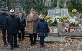 Zdjęcie przedstawia grupę os&oacute;b stojących przy nagrobkach na Cmentarzu Powązkowskim