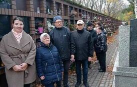 Zdjęie przedstawia grupę os&oacute;b stojących przy nagrobkach w Alei Zasłużonych na Powązkach