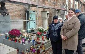 Zdjęie przedstawia grupę os&oacute;b stojących przy nagrobkach w Alei Zasłużonych na Powązkach