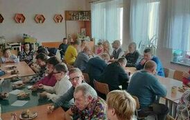 Zdjęcie przedstawia grupę os&oacute;b siedzących przy stołach i degustujących słodkości
