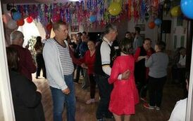 Na zdjęciu grupa kobiet i mężczyzn tańczących na sali udekorowanej kolorowymi balonami i paskami z bibuły
