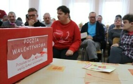 Zdjęcie przedstawia pudełko z kartkami walentynkowymi, w tle siedzą kobiet i mężczyźni