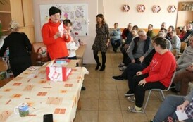 Kobieta trzymająca kartkę walentynkową, obok grupa os&oacute;b siedzących na krzesłach podczas spotkania walentynkowego