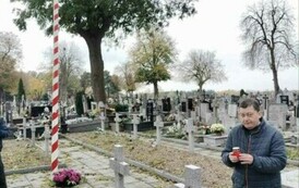 Mężczynza trzymający znicz przy grobach Żołnierzy poległych na cmentarzu wojennym