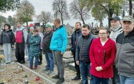 Grupa kobiet i mężczyzn stojących przy grobach Żołnierzy poległych na cmentarzu wojennym