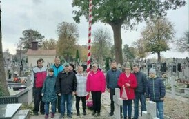 Grupa kobiet i mężczyzn stojących przy grobach Żołnierzy poległych na cmentarzu wojennym