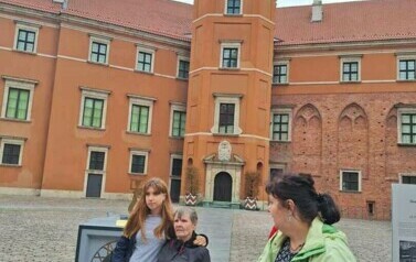 Trzy kobiety stoją na tle Zamku Kr&oacute;lewskiego w Warszawie