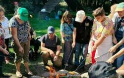 Na zdjęciu grupa kobiet i mężczyzna piekących kiełbaski przy ognisku 