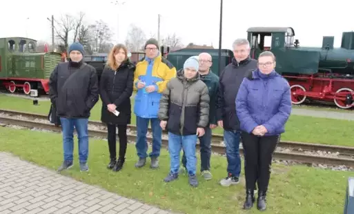 Grupa kobiet i mężczyzn stojących na tle kolejki w Muzeum Kolei Wąskotorowej w Sochaczewie.